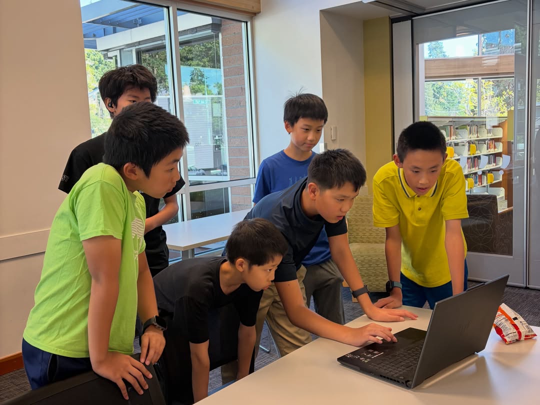 Five students crowded around one laptop at a library table